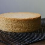 A freshly baked sponge cake resting on a cooling rack, showcasing its golden crust.
