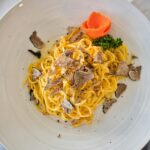 Delicious gourmet pasta served with truffle shavings and a vibrant garnish on a white plate.