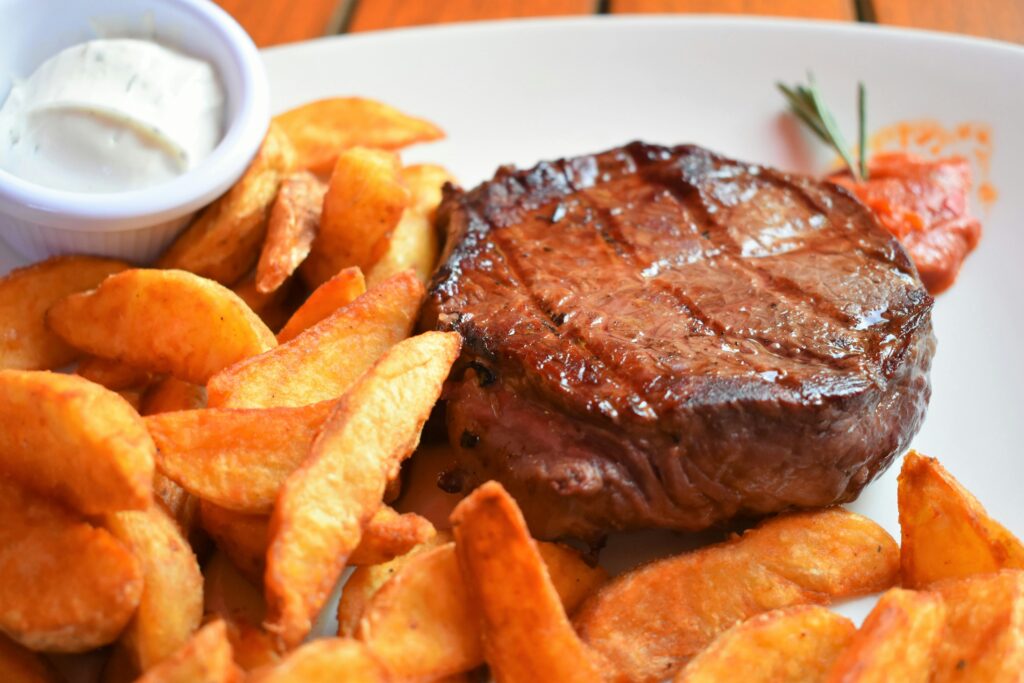 Delicious grilled steak with crispy potato wedges and dipping sauce, perfect for a hearty meal.
