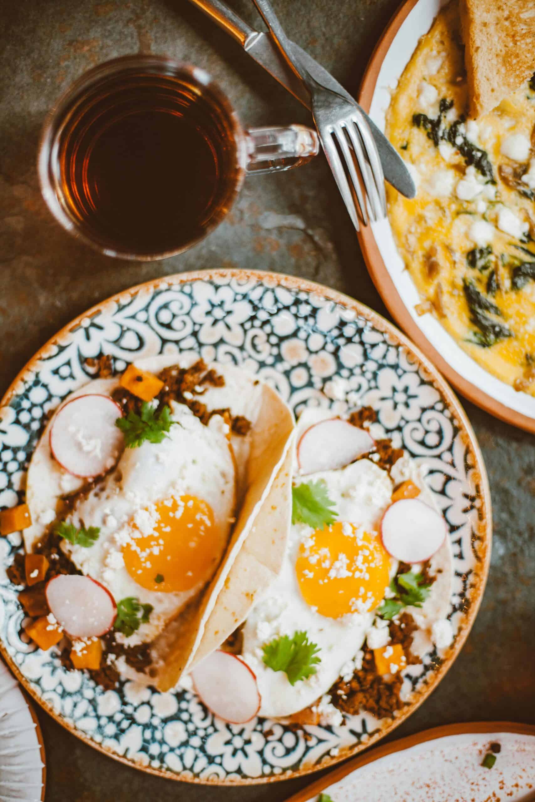 Explore a vibrant breakfast spread featuring sunny side up tacos with radishes and a glass of dark beverage.