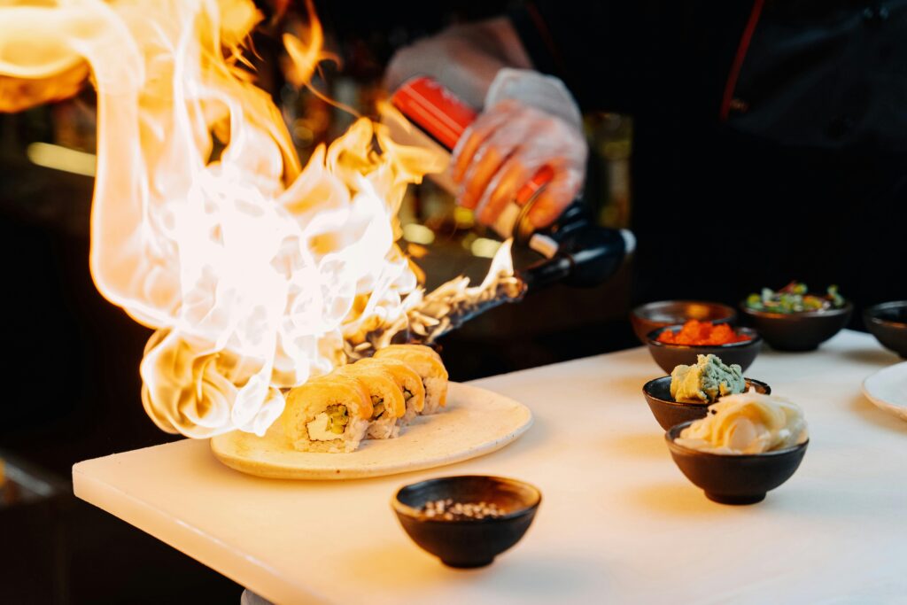 Chef using a blow torch to prepare sushi, showcasing culinary skills and Japanese cuisine.