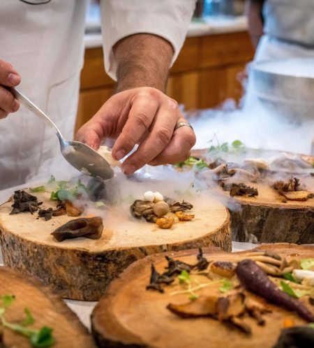 A chef artfully plating a gourmet dish with mushrooms and greens on wood slices. best aesthetic cafe